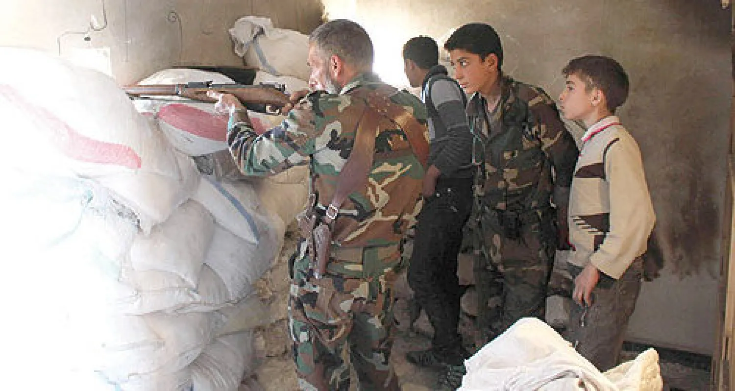 أحد عناصر الجيش الحر يشرح لمقاتلين صغار كيفية التصويب في منطقة الشيخ سعيد بحلب أمس (رويترز)