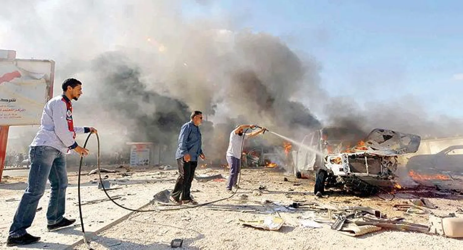 ليبيون يطفئون نيرانا اشتعلت في سيارة مفخخة بعد تفجيرها بجوار مركز انتخابي في بنغازي أمس (رويترز)