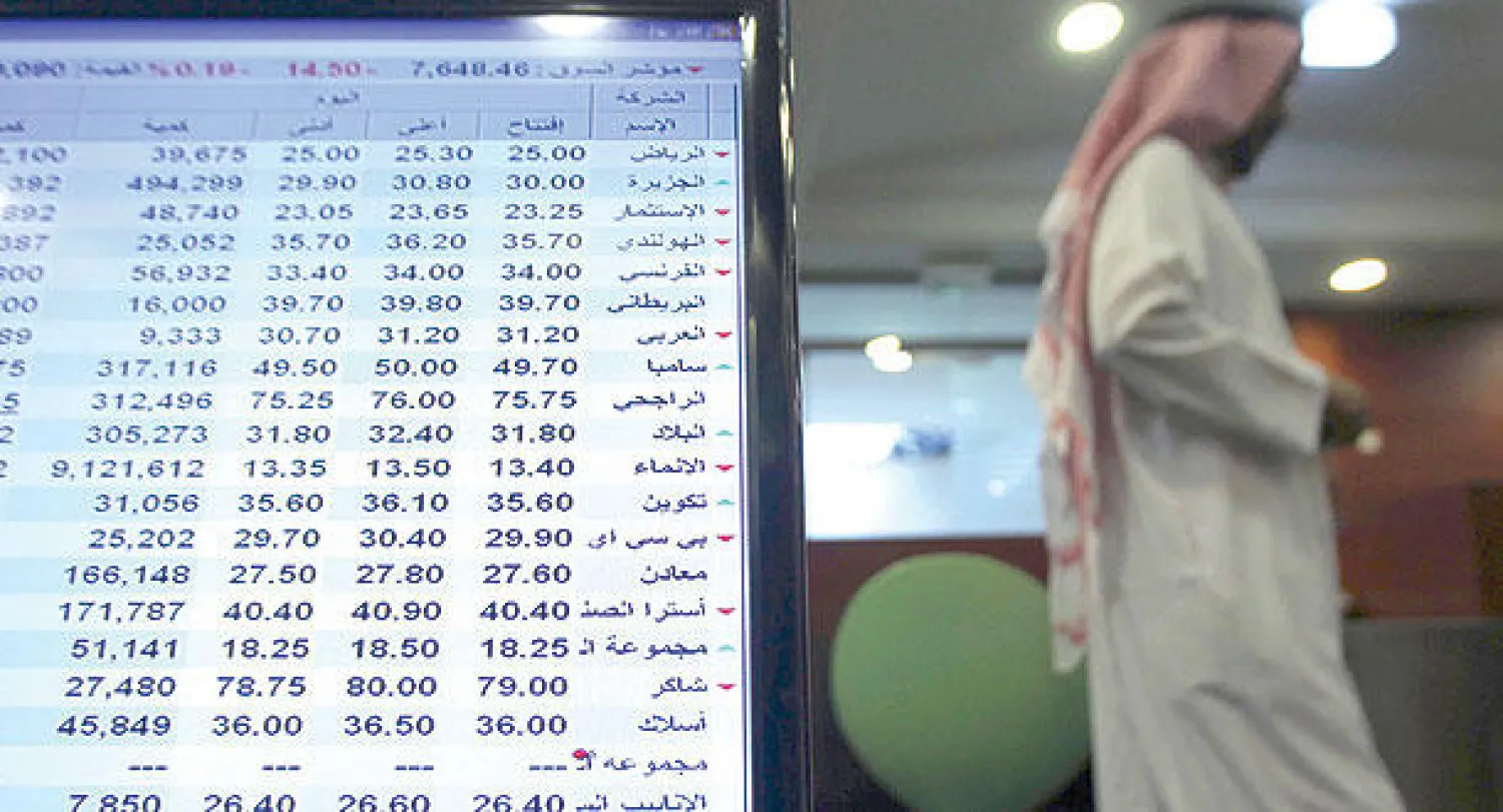 متعامل في البنك السعودي للاستثمار  بينما تبين شاشة عرض مؤشر سوق الأوراق المالية في الرياض (رويترز)