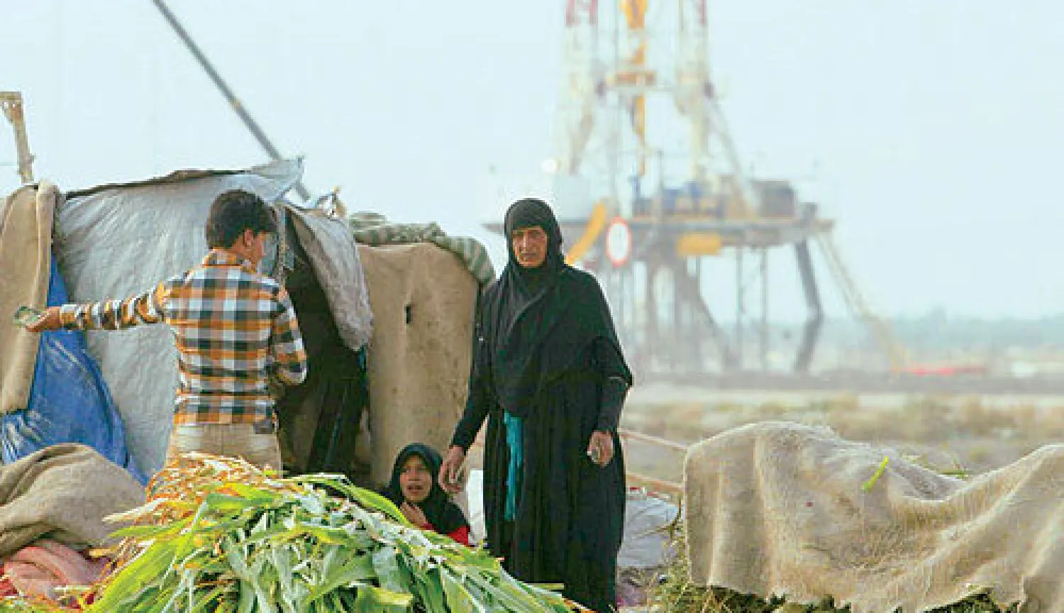 قروية تقف قرب مسكنها في البصرة حيث يبدو برج النفط في حقل (غرب القرنة 2) قريبا منها (رويترز)