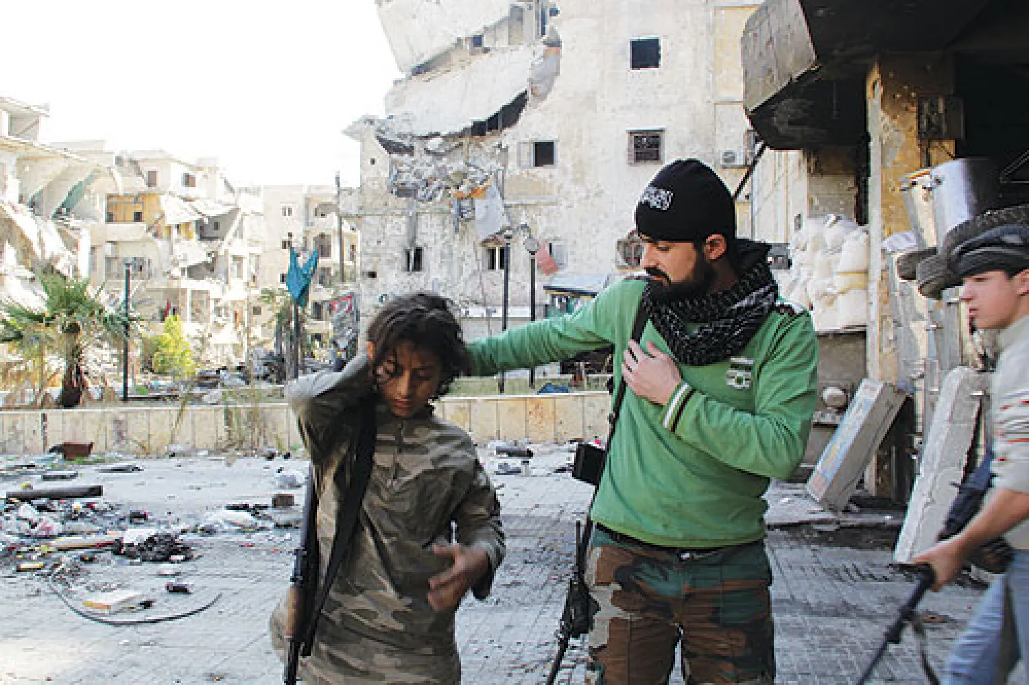 مقاتل سوري يساعد صبيين قبل انطلاقهم في دورية في حي صلاح الدين بمدينة حلب أمس (أ.ف.ب)