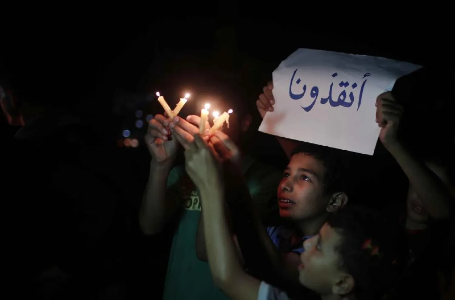 اطفال فلسطينيون في غزة يحملون شموعا ولافتة كتب عليها انقذونا