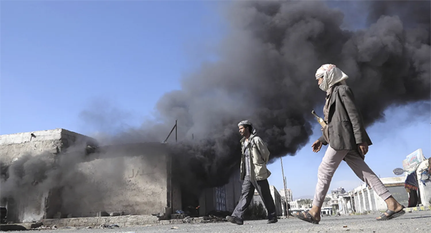 يمنيون يسيرون قرب أدخنة صادرة عن حريق اندلع في العاصمة صنعاء اليوم (رويترز) 