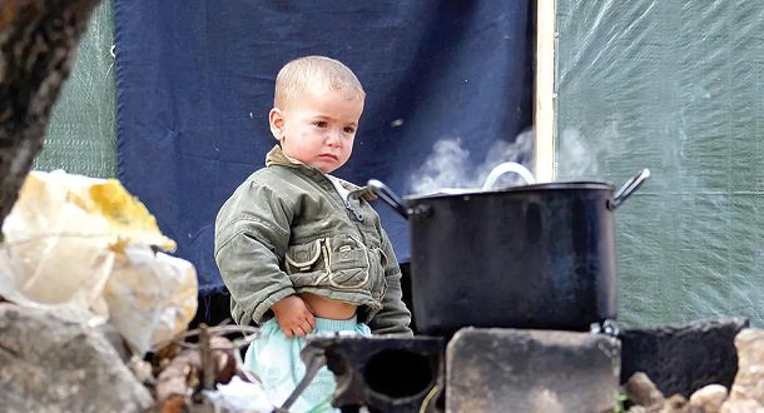 طفل سوري من اللاجئين الذين قدموا من حلب يقف إلى جانب طنجرة طبخ، في أحد الملاجئ بلبنان، أمس (إ.ب.أ)