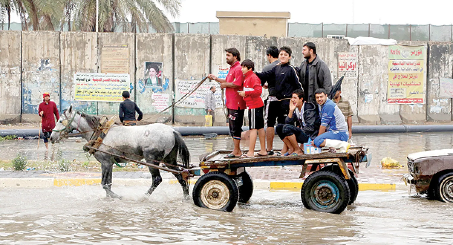 عراقيون يتنقلون وسط بغداد بواسطة عربة يجرها حصان بسبب غرق شوارع العاصمة العراقية بمياه الأمطار (أ.ب)
