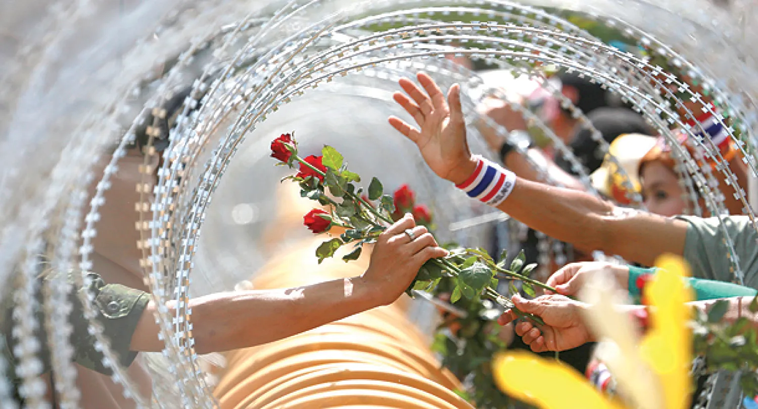 متظاهر يقدم وردا إلى جندي خلال مسيرة مناهضة للحكومة قرب وزارة الدفاع في بانكوك أمس (أ.ب)