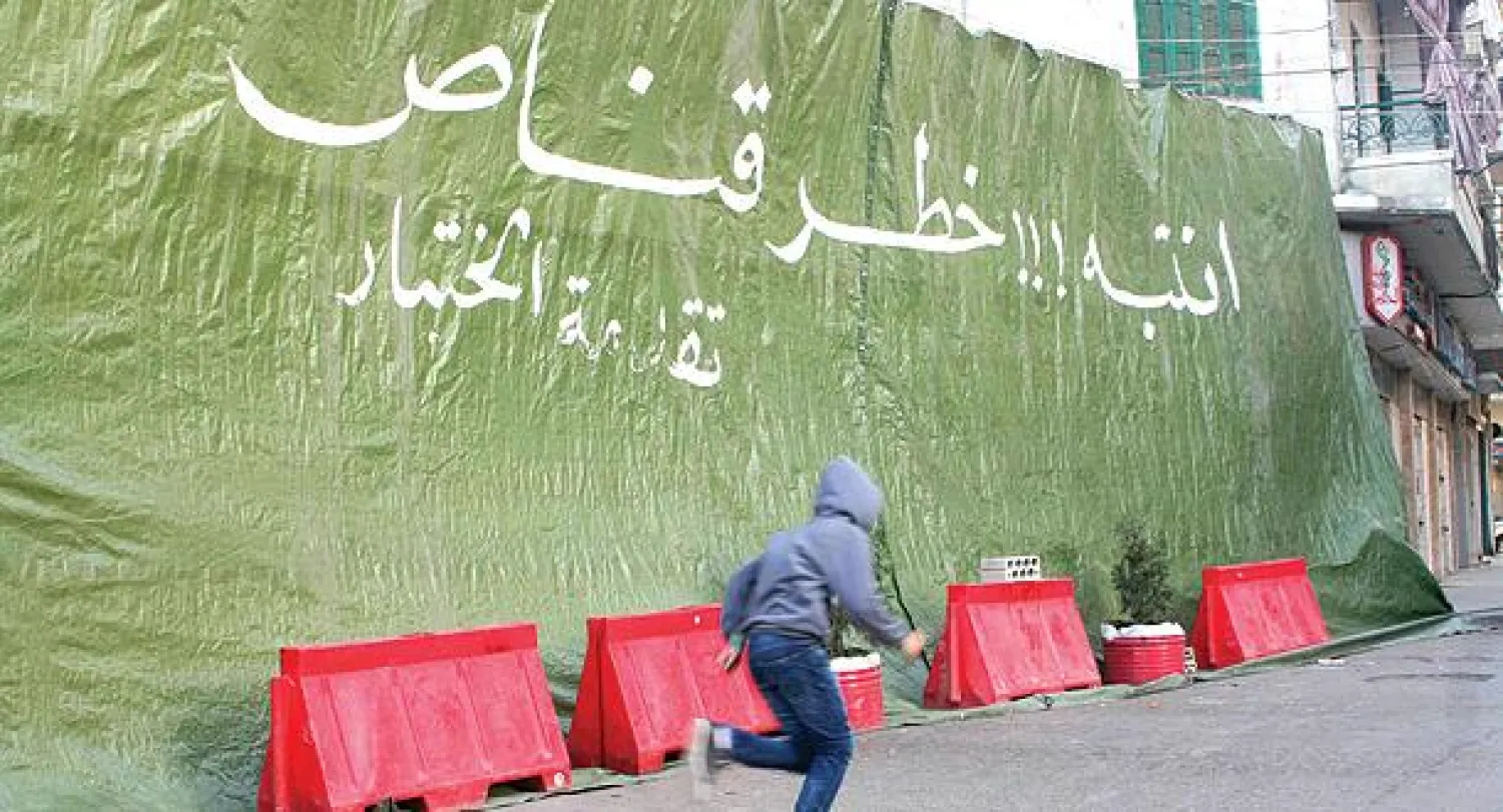 صبي لبناني يركض مسرعا لتفادي القناصة بينما تحذر لافتة كبيرة من نيرانهم في طرابلس أمس (رويترز)