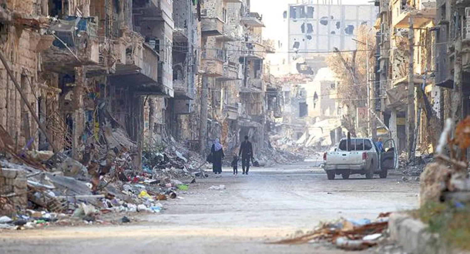 مقاتل في الجيش السوري الحر يسير مع أسرته بين الأنقاض في شارع بمدينة دير الزور (رويترز)