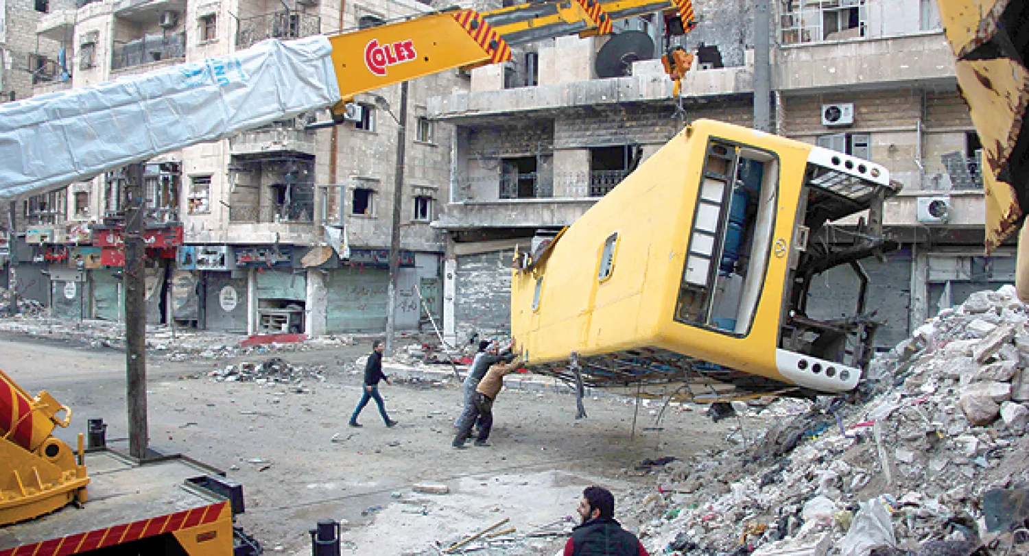 مقاتلون سوريون يحاولون رفع حافلة مدمرة لبناء حواجز قتالية في حي صلاح الدين بمدينة حلب أمس (أ.ف.ب)