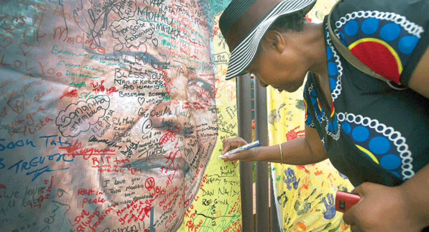 امرأة من مدينة سويتو بجنوب أفريقيا توقع بالتعزية على ملصق ضخم حمل صورة نيلسون مانديلا، الذي توفي أول من أمس (أ.ب)