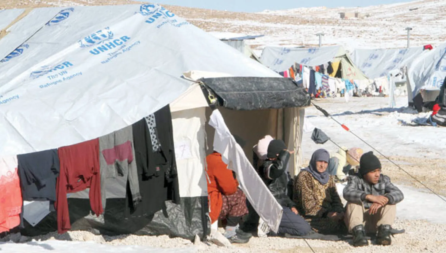 أسرة سورية تجلس بجانب خيمتها في معسكر للاجئين ببلدة عرسال الحدودية في البقاع الشرقي (رويترز)
