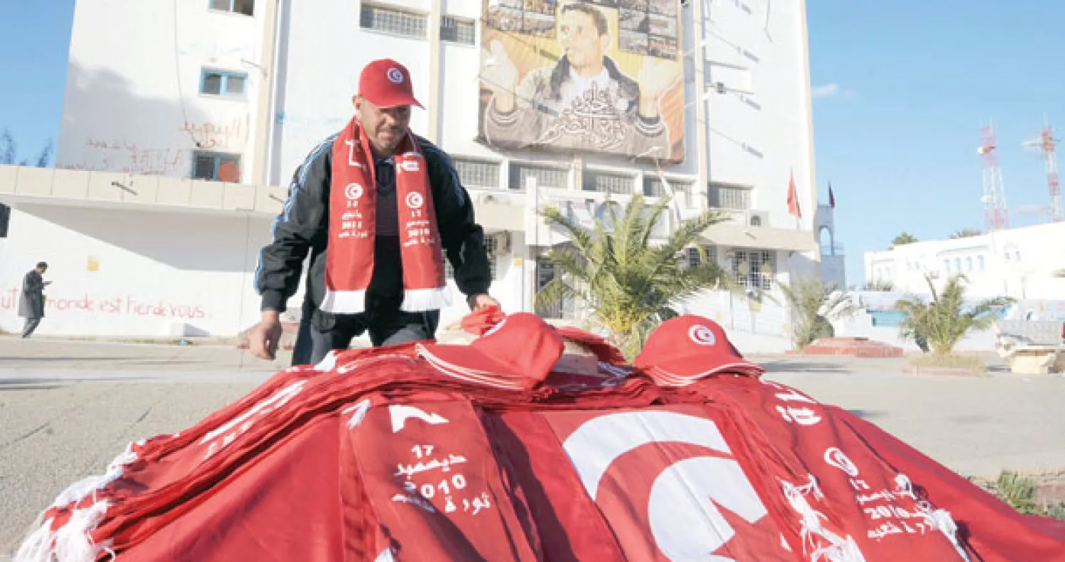 بائع تونسي يعرض أعلاما وقبعات في ساحة محمد البوعزيزي بسيدي بوزيد بمناسبة احتفالات انطلاق الثورة في تونس (أ.ف.ب)