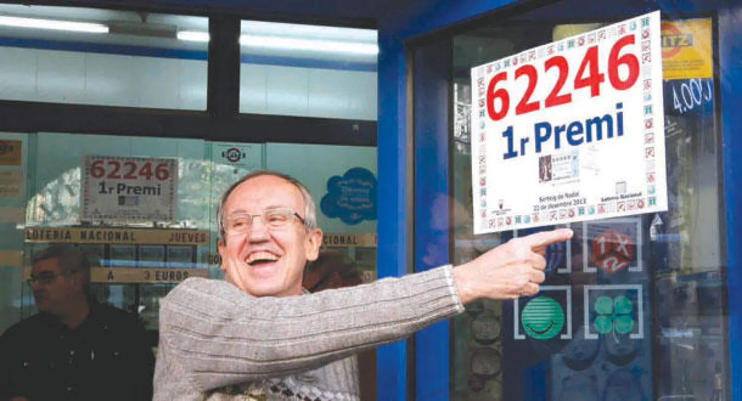 صاحب متجر يشير إلى الرقم الفائز بالجائزة الأولى في إسبانيا (رويترز)
