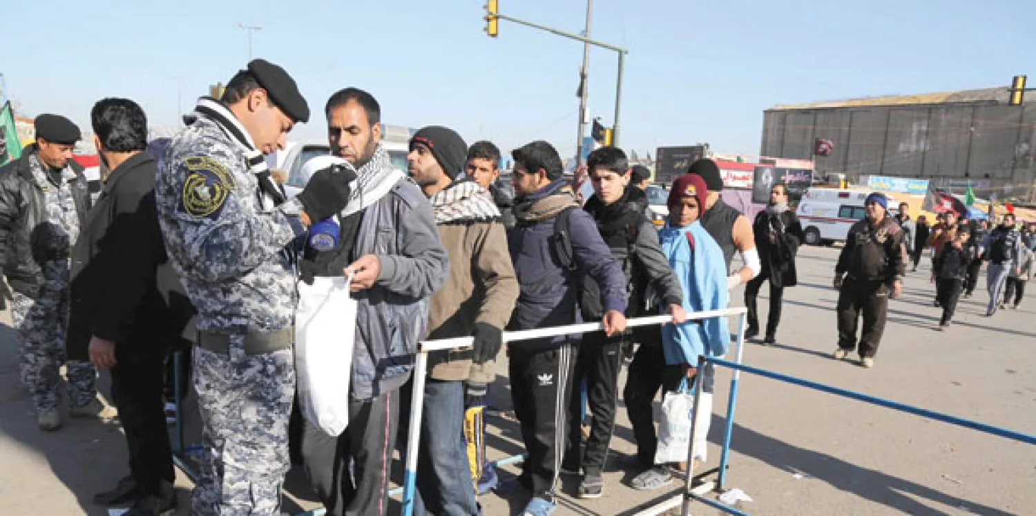 شرطي يفتش زوارا في طريقهم إلى كربلاء أمس للمشاركة في إحياء ذكرى أربعينية الإمام الحسين (أ.ب)