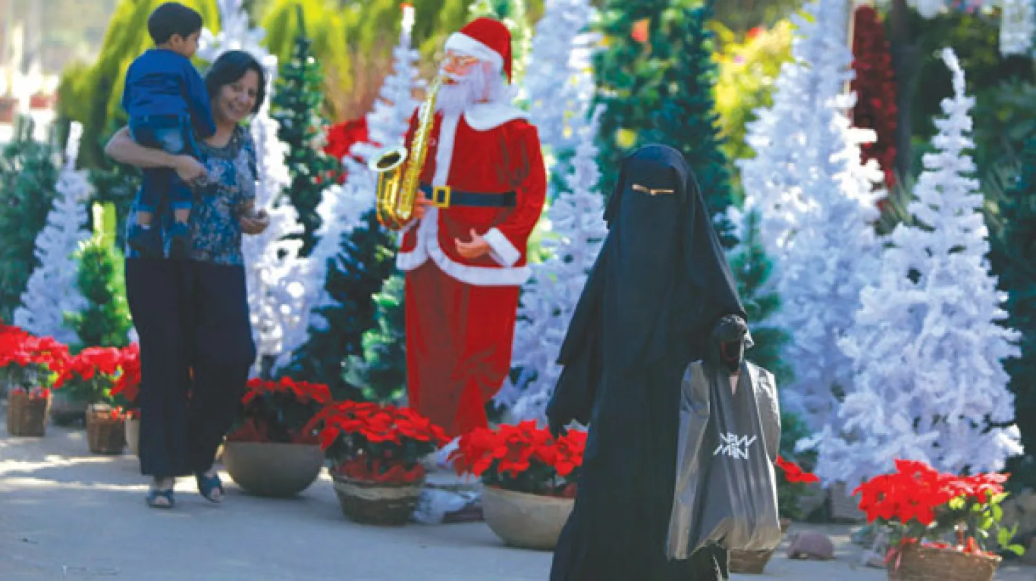 متنقبة مصرية تمر بينما أخرى تتطلع مع ابنها إلى زينات رأس العام في أحد شوارع القاهرة (أ.ب)