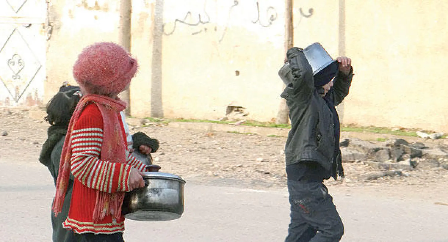 أطفال سوريون يحملون قدورا فارغة بحثا عن الطعام في أحد شوارع الغوطة الشرقية قرب دمشق (رويترز)