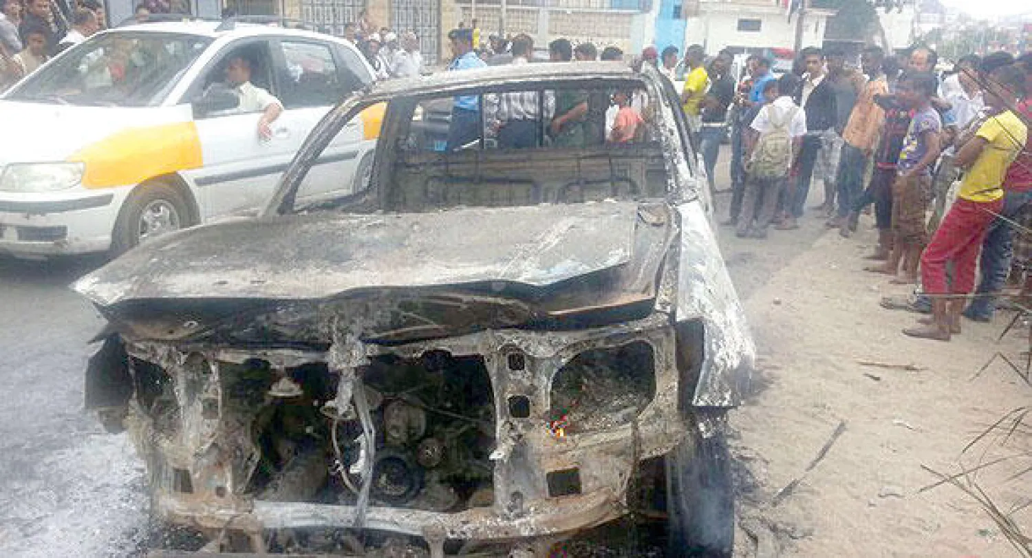 يمنيون يتجمهرون حول حطام سيارة تعرضت لهجوم بقنبلة مما أدى إلى إصابة ضابط كبير في الجيش في عدن أمس (أ.ف.ب)