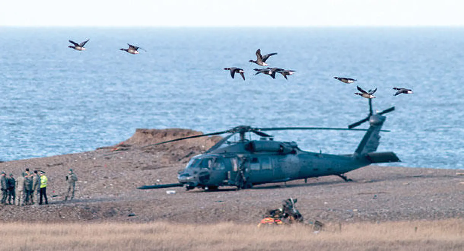 ضباط يتحدثون بينما تحلق طيور قرب موقع تحطم الهليكوبتر  في نورفولك بالساحل الشرقي لإنجلترا، أمس (إ.ب.أ)