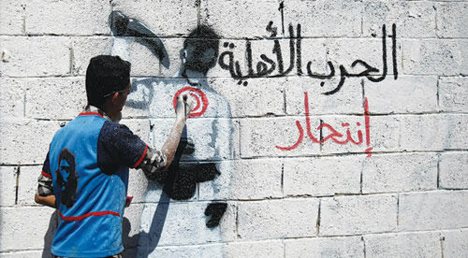 ناشط يمني يكتب على جدار في أحد الشوارع أثناء حملة ضد «الحرب الأهلية» في العاصمة صنعاء أمس (أ. ف. ب)