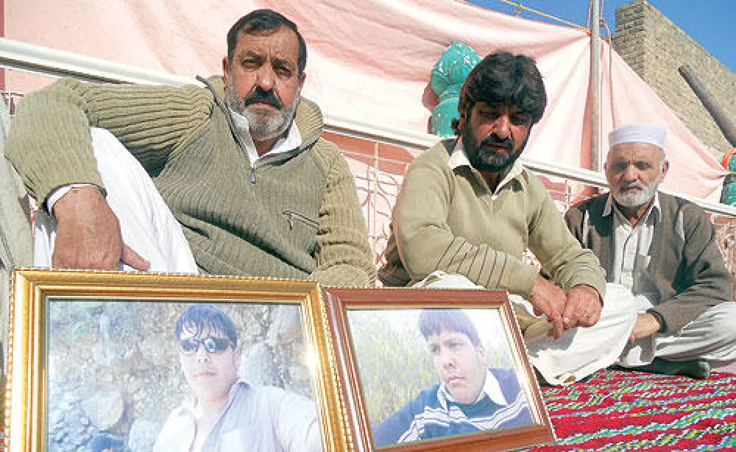 مجاهد علي (يسار) يضع صورتين لابنه اعتزاز حسن، خلال جلسة عزاء في بلدة هانغو بشمال شرقي باكستان أمس (أ.ف.ب)