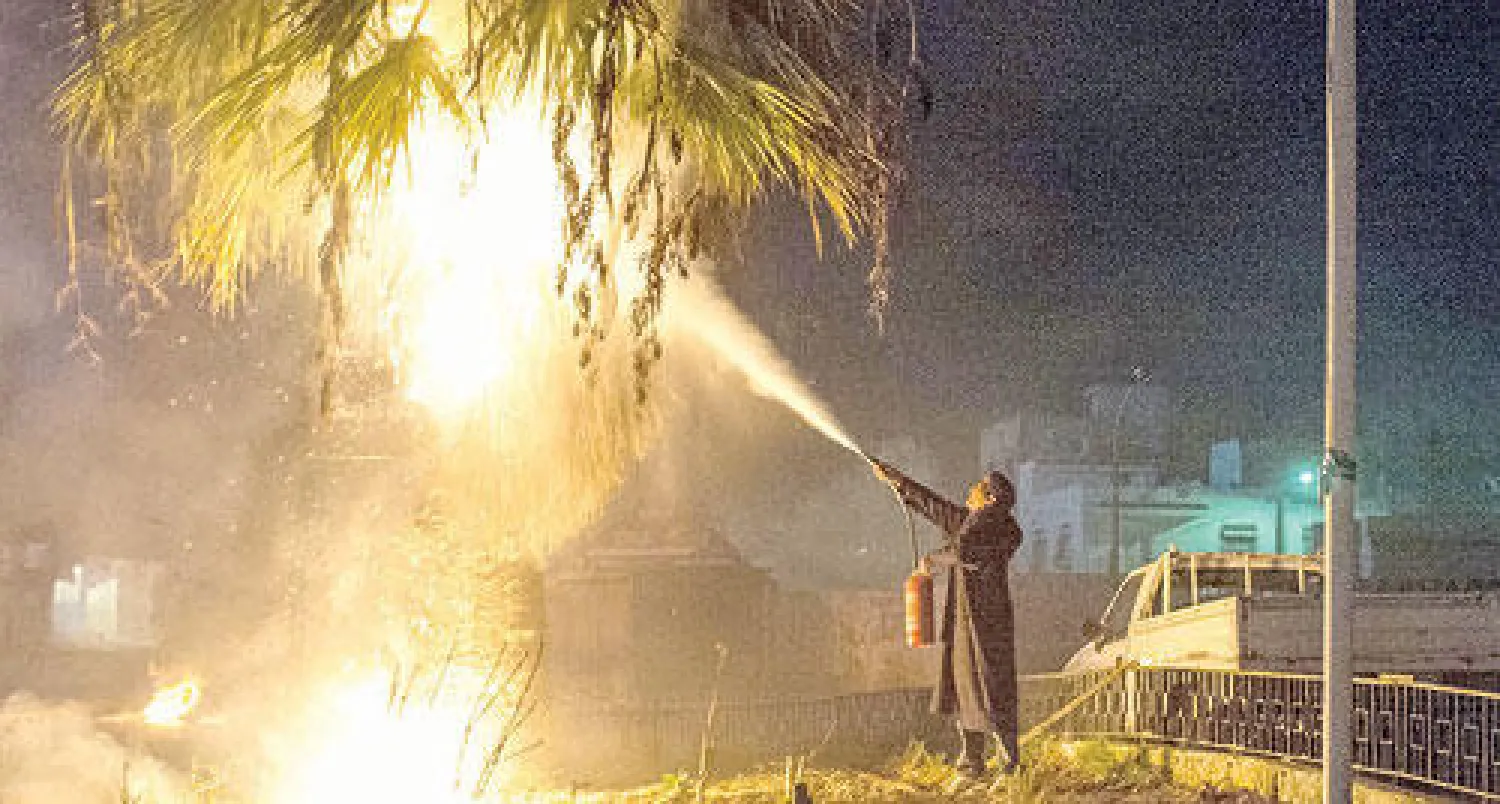 رجل أمن يطفئ نيرانا أضرمت في إحدى الأشجار بعد أعمال الشغب التي شهدتها منطقة «حي التضامن» غرب تونس العاصمة ليلة الجمعة (أ.ب)