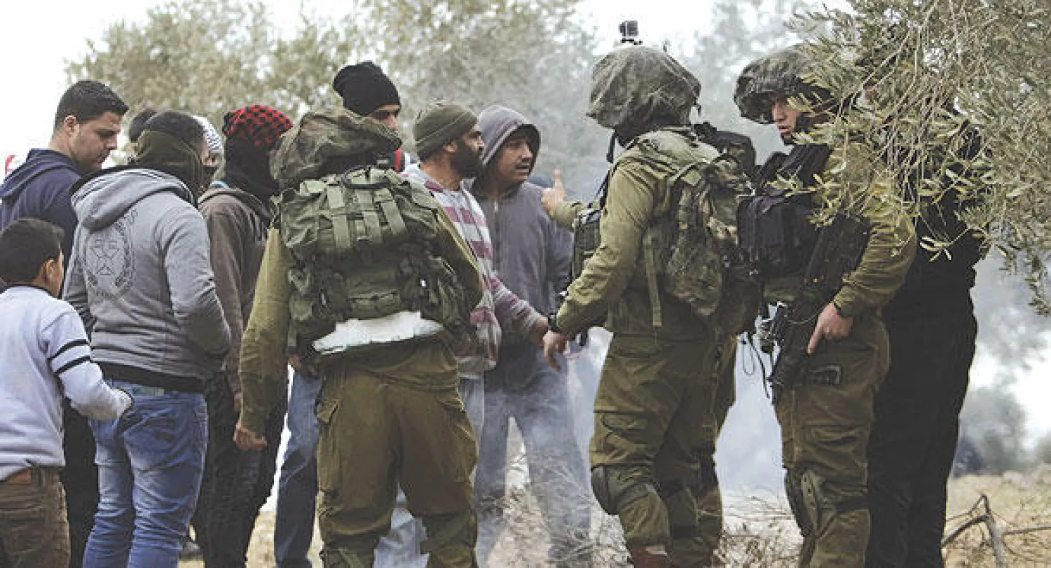 جنود إسرائيليون يتحدثون إلى مزارعين فلسطينيين بعد مواجهات  مع مستوطنين في قرية بالضفة الغربية أمس (أ.ب)