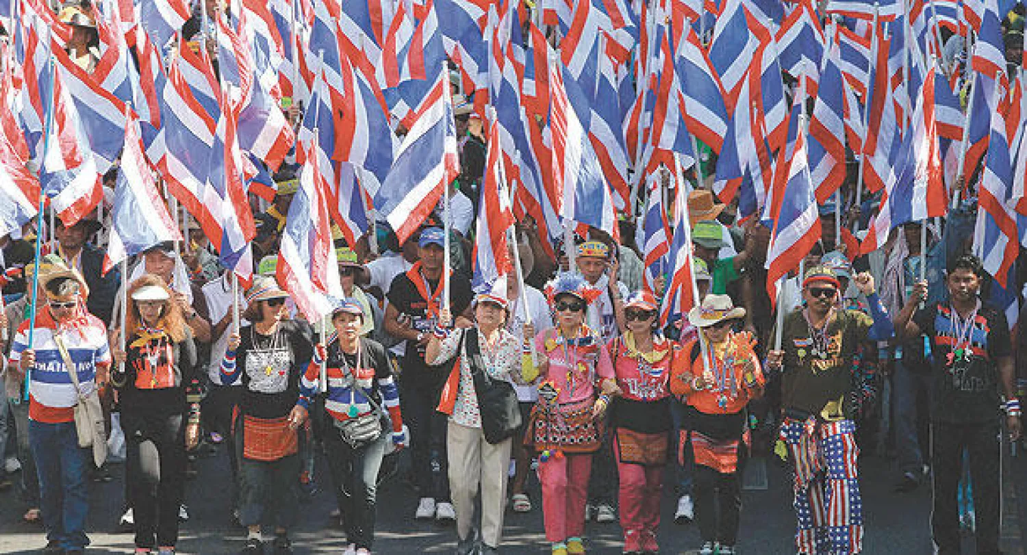 مناهضون للحكومة يحملون الأعلام الوطنية خلال تظاهرهم في بانكوك أمس (رويترز)