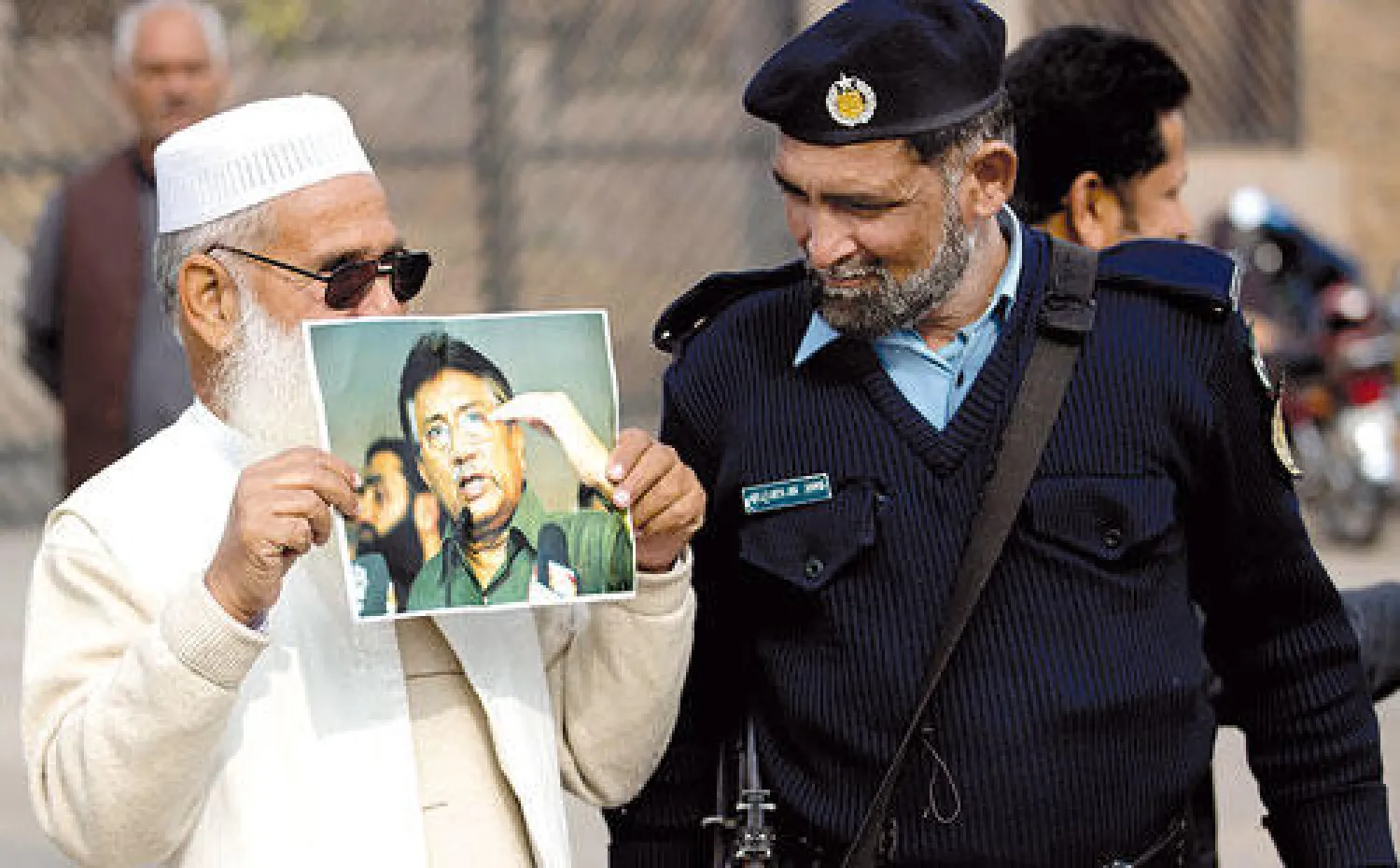 شرطي ينظر إلى صورة لمشرف يحملها أحد أنصاره خارج المحكمة في إسلام آباد، أمس (أ.ب)