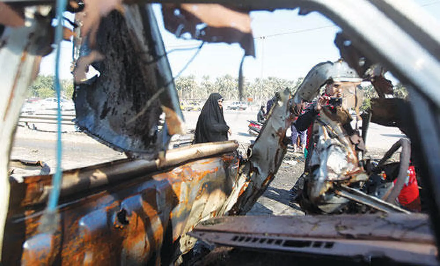 عراقية تمر بجانب حطام سيارة في موقع انفجار بمنطقة الطوبجي ببغداد أمس (أ.ف.ب)