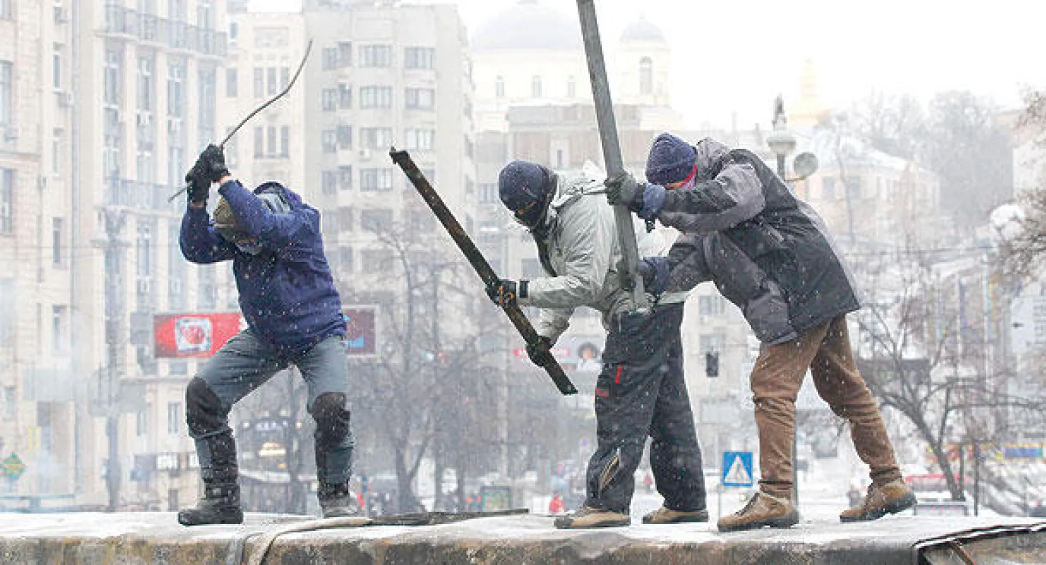 متظاهرون موالون لأوروبا يضربون بهراواتهم عربة محترقة وسط استمرار الاحتجاجات في كييف أمس (رويترز)