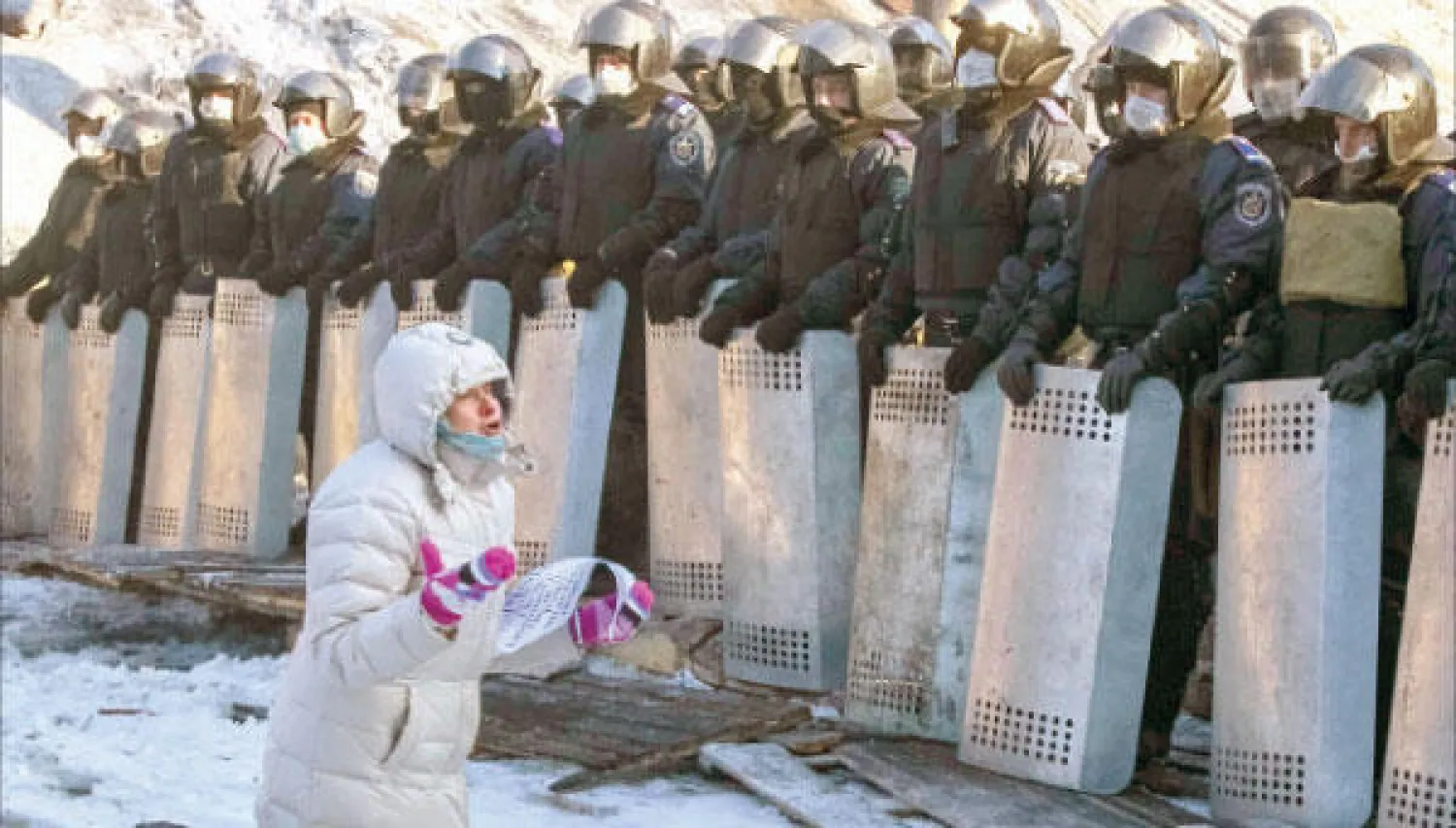 امرأة تجثم على ركبتيها مناشدة قوات مكافحة الشغب في موقع شهد مواجهات مع محتجين مناهضين للحكومة في كييف أمس (رويترز)