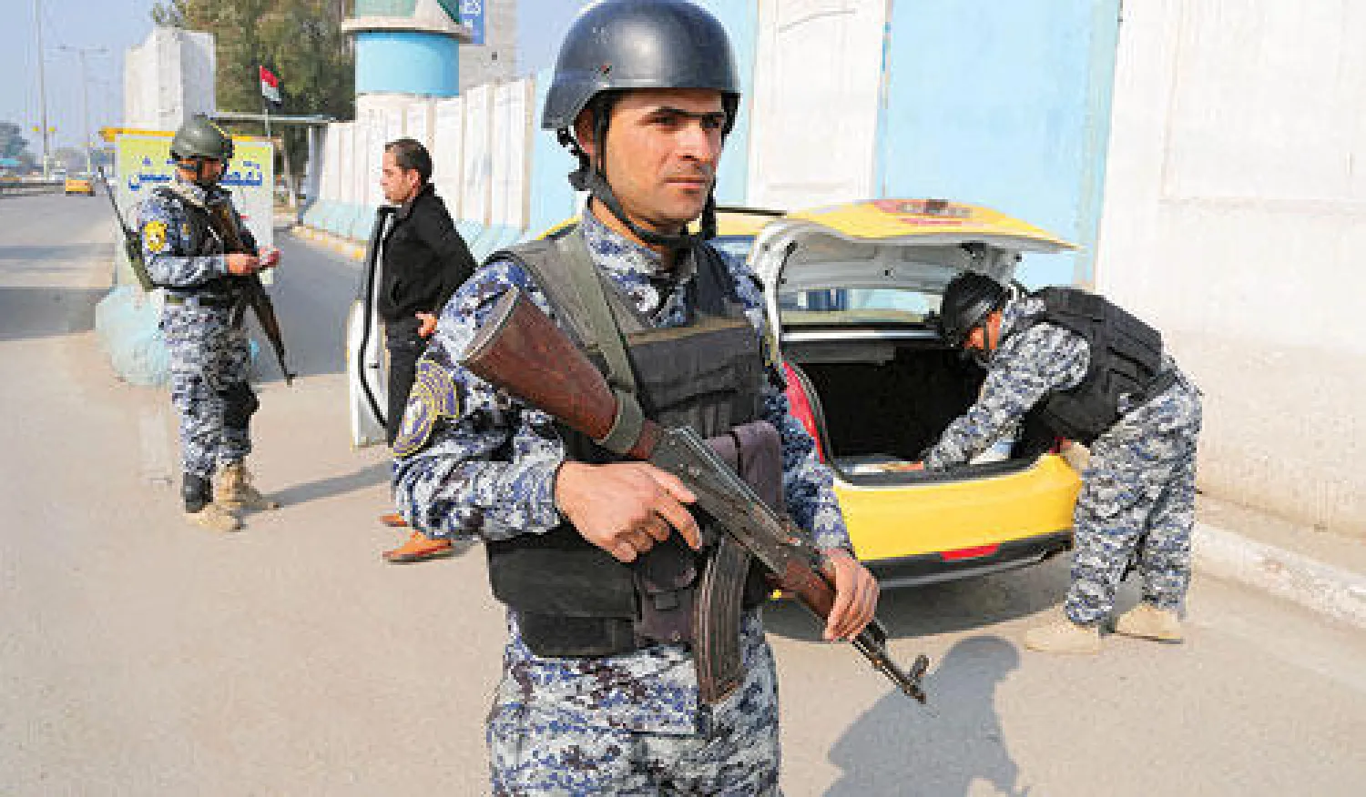 شرطي عراقي يقف في حالة تأهب وهو يحمل سلاحه بينما زميلاه يفتشان سيارة أجرة في نقطة تفتيش وسط بغداد أمس (أ.ب)