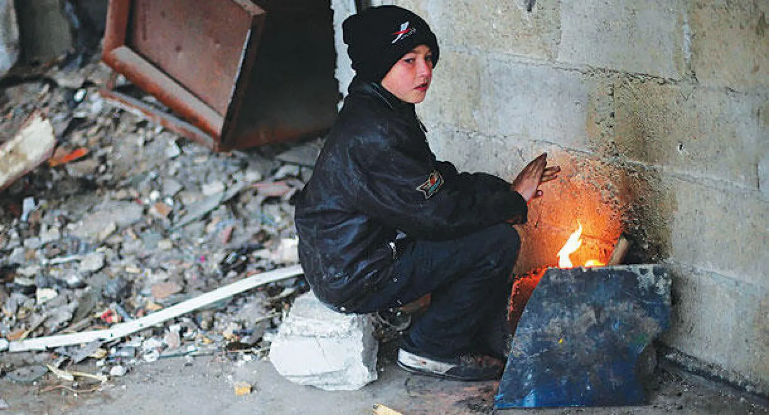 طفل سوري يجلس في منزل مهدم في حي دوما القريب من العاصمة دمشق أمس (رويترز)