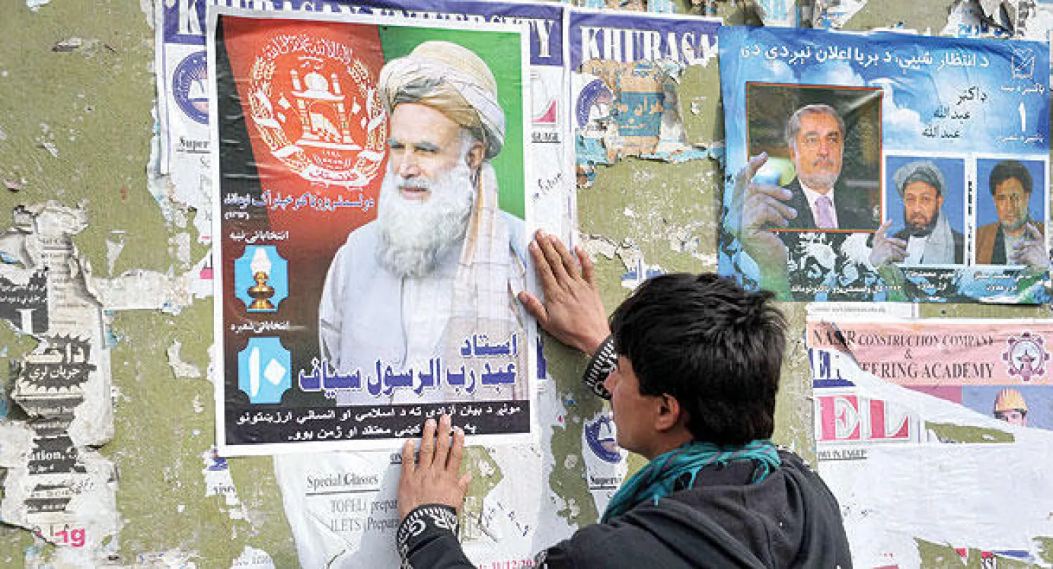 أفغاني يعلق صورة دعائية للمرشح الرئاسي عبد رب الرسول سياف بمدينة جلال آباد أمس (أ.ف.ب)