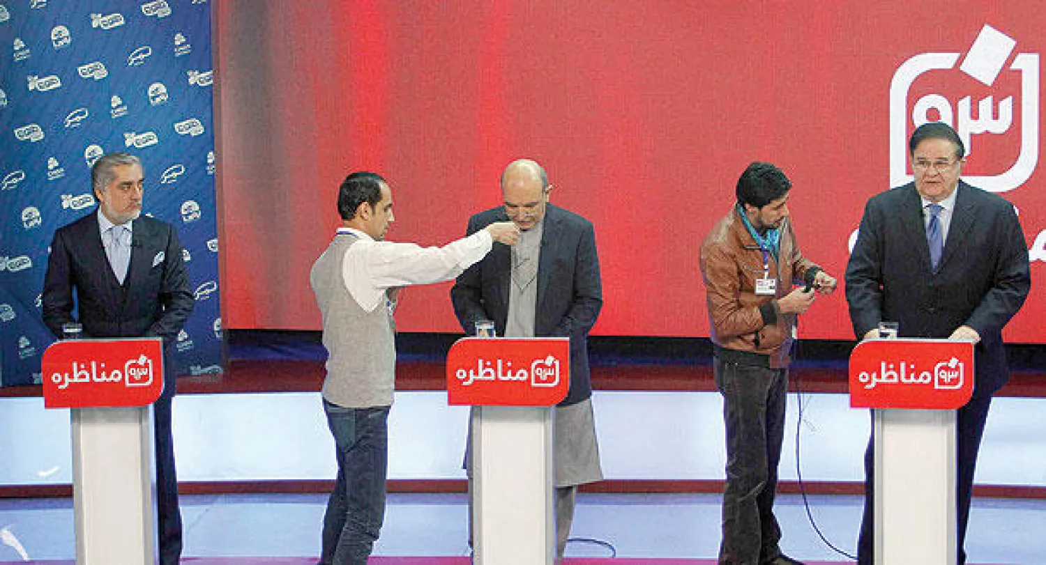 رجلان من الشبكة الإخبارية المنظمة للمناظرة يساعدان في وضع المايكروفون في ملابس المرشحين  عبد الرحيم ورداك (يمين) وعبد القيوم كرزاي (وسط) قبل انطلاق النقاش في كابل الليلة قبل الماضية (رويترز)