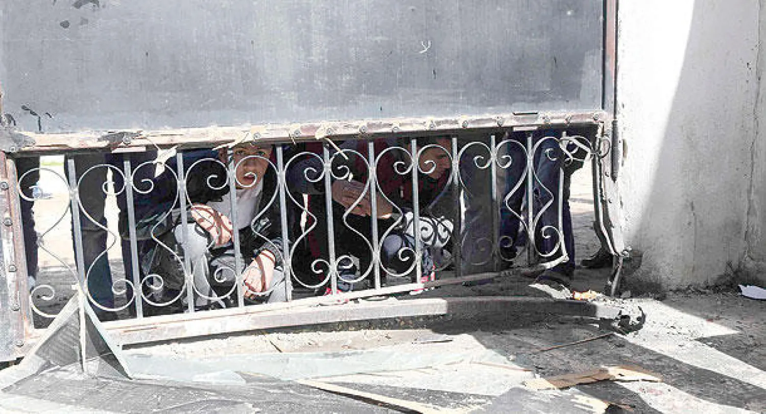 تلاميذ ليبيون مختبئون وراء بوابة مدرسة في بنغازي بعد ان رمى مجهول قنبلة يدوية داخلها (رويترز)