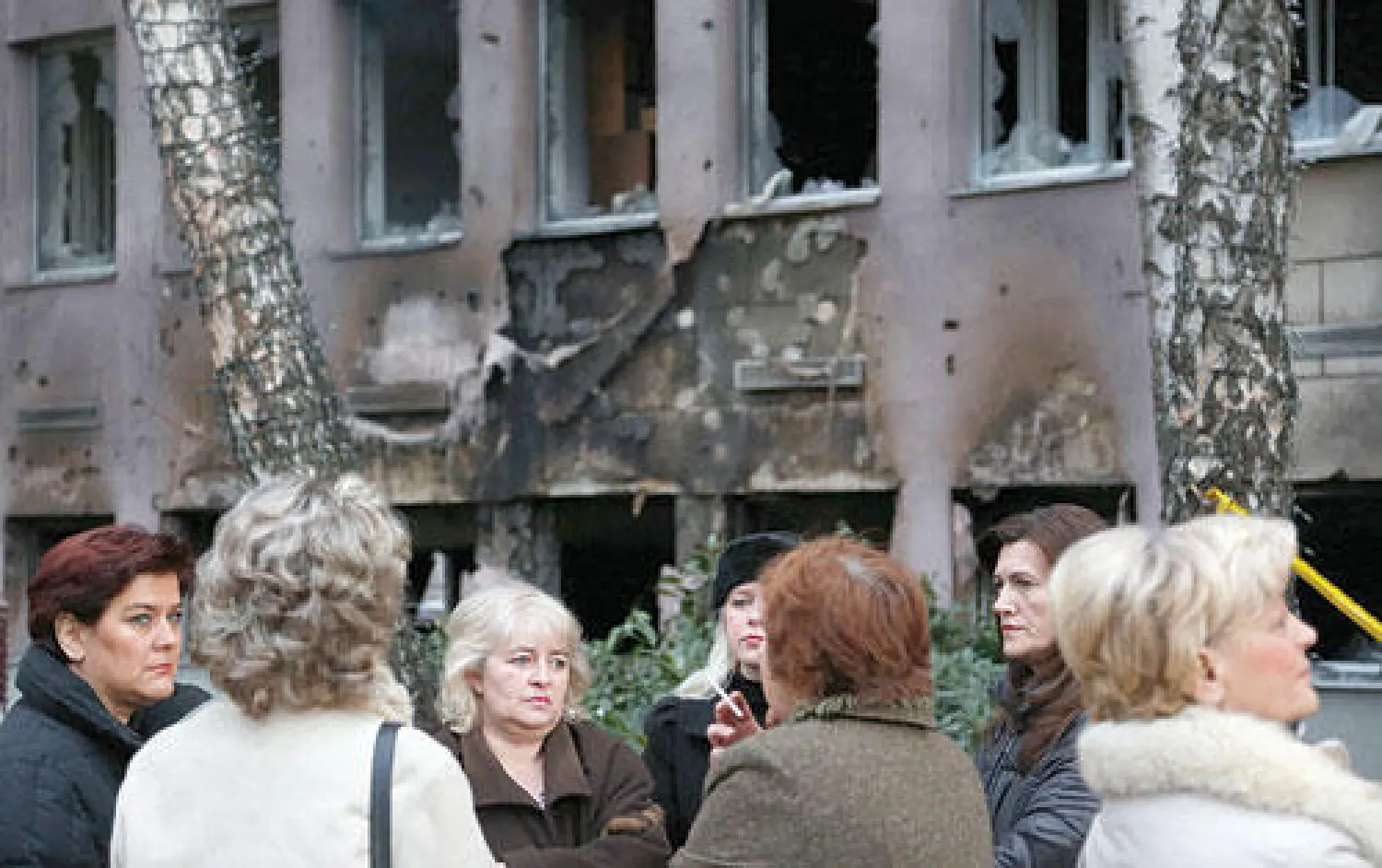 موظفات بوسنيات يقفن أمام مبنى حكومي طالته النيران خلال الاحتجاجات في توزلا أمس (أ.ب)