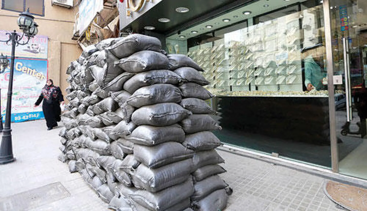 لبنانية تسير بمحازاة أكياس رمل أمس وضعت لحماية المحال التجارية من انفجارات السيارات المفخخة (رويترز)