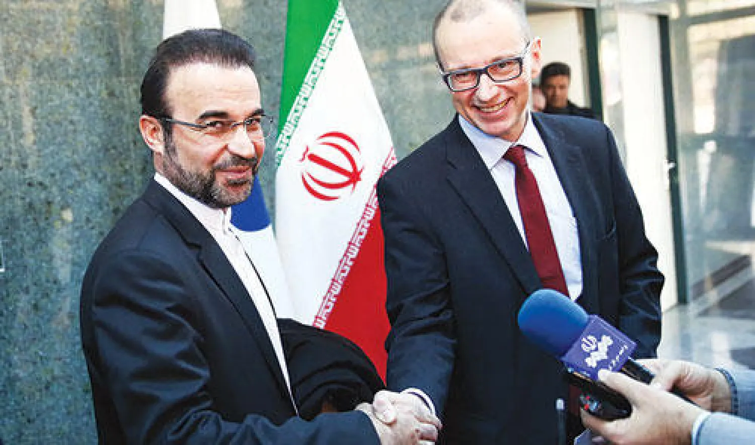 نائب رئيس الوكالة الذرية تيرو فاريورنتا يصافح المندوب الايراني رضا نجفي في طهران بعد توقيع الاتفاق أمس (إ ب أ)