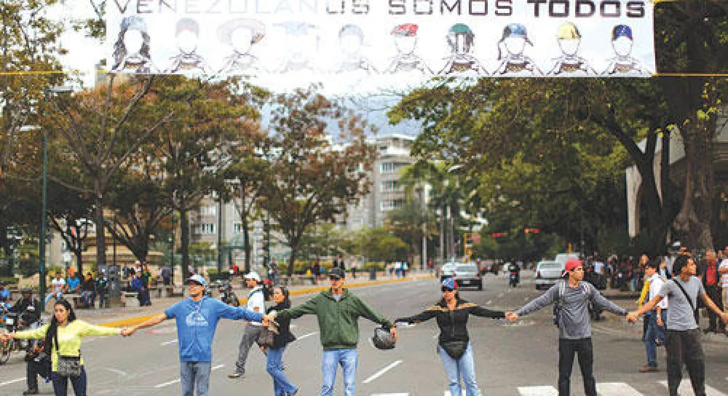 متظاهرون يقطعون طريقا رئيسا في العاصمة الفنزويلية وتعلوهم لافتة مكتوب عليها «كلنا فنزويلا» (أ.ب)