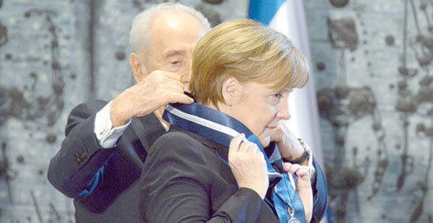 الرئيس الإسرائيلي شيمعون بيريس يقلد المستشارة الألمانية أنجيلا ميركل وسام رئيس الدولة في القدس أمس (إ.ب.أ)