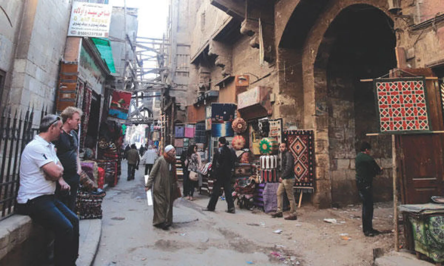 سائحان غربيان يجلسان للاستراحة على أحد الأسوار بمنطقة خان الخليلي السياحية وسط القاهرة أمس (إ.ب.أ)