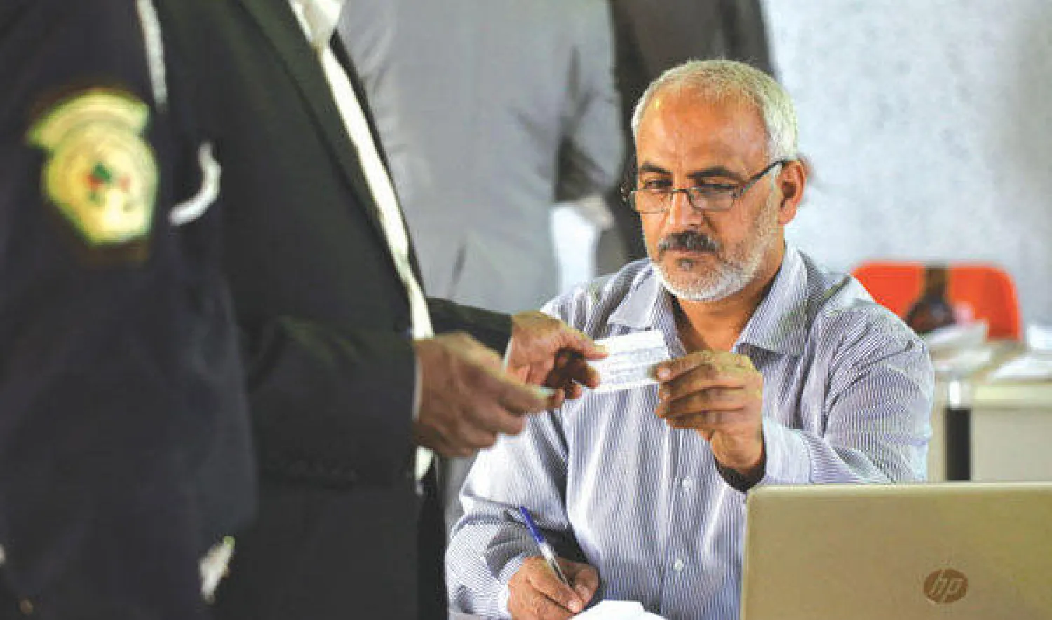 موظف بمفوضية الانتخابات العراقية يقوم بتسليم بطاقة هوية الناخب الإلكترونية لشرطي عراقي في النجف أمس (أ.ف.ب)