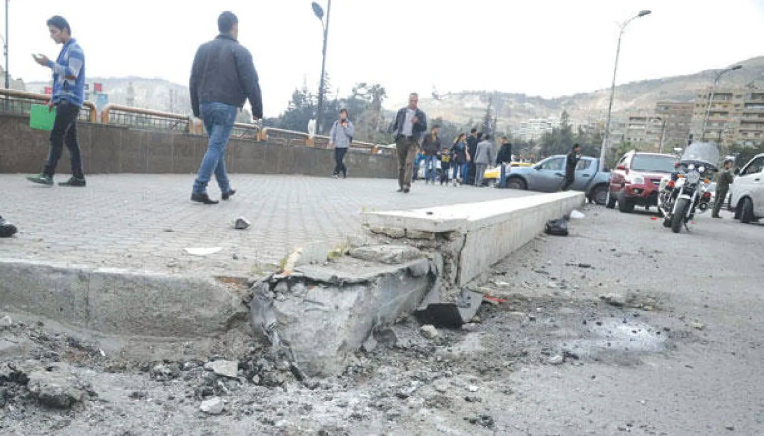 سوريون يسيرون على رصيف في ساحة الأمويين بدمشق تعرض لأضرار بعد سقوط قذيفة هاون (رويترز)