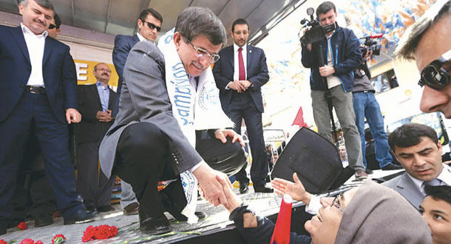 داود أوغلو يستمع لسيدة تركية خلال حملته الانتخابية الداعمة لحزبه (العدالة والتنمية) في مدينة قونيا التركية أمس (أ.ف.ب)