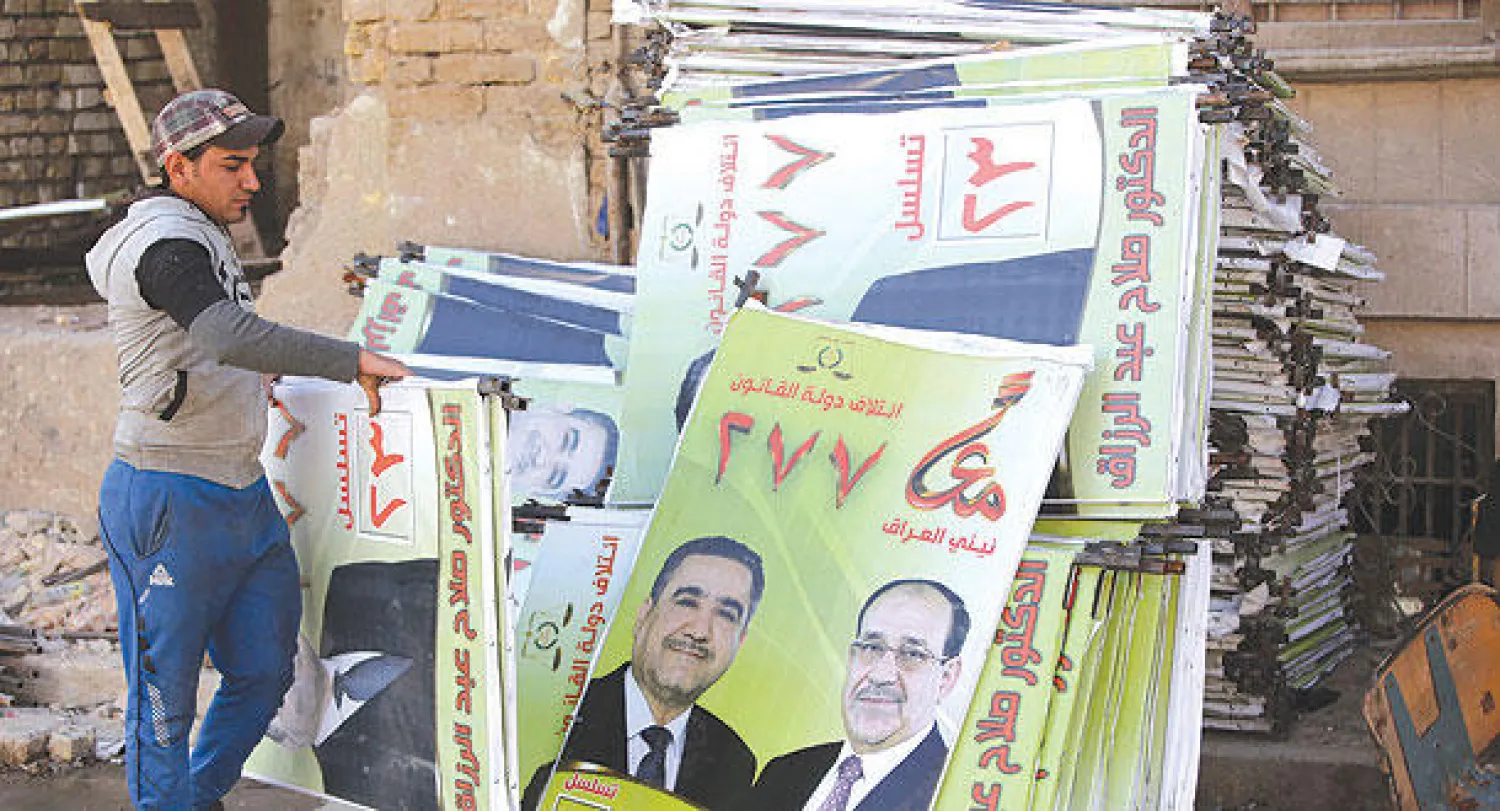 عامل يجمع ملصقات دعائية عليها صورة الرئيس الوزراء نوري المالكي ومحافظ بغداد السابق صلاح عبدالرزاق وسط العاصمة العراقية أمس (أ.ف.ب)