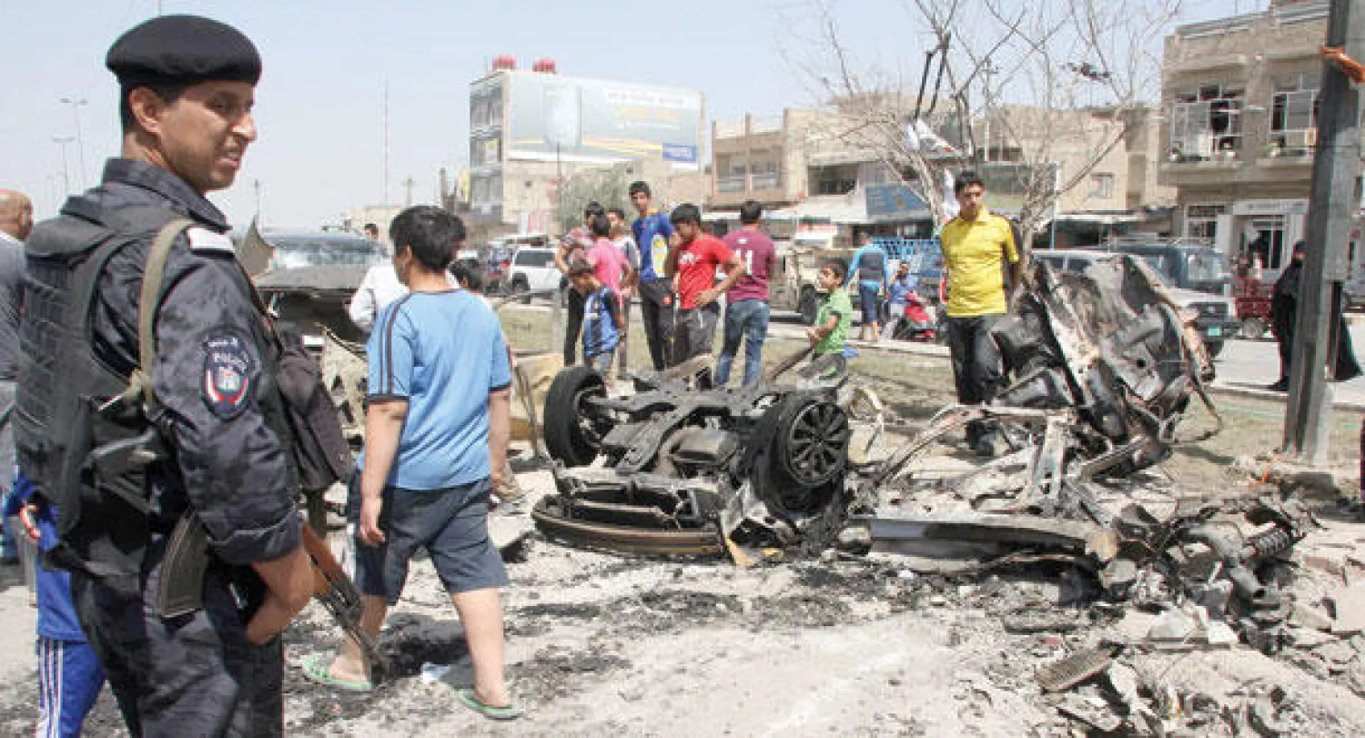 شرطي ومدنيون في موقع انفجار سيارة مفخخة ببغداد أمس (رويترز)
