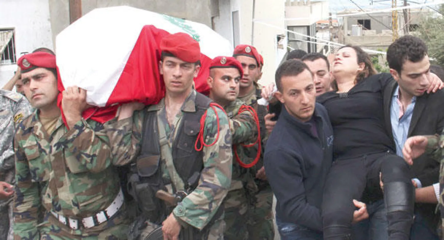 جنود لبنانيون يحملون أمس نعش ضابط لقي حتفه بنيران مسلح.. بينما يحمل آخرون والدته التي لم تقو على السير خلال تشييعه في عكار (رويترز)