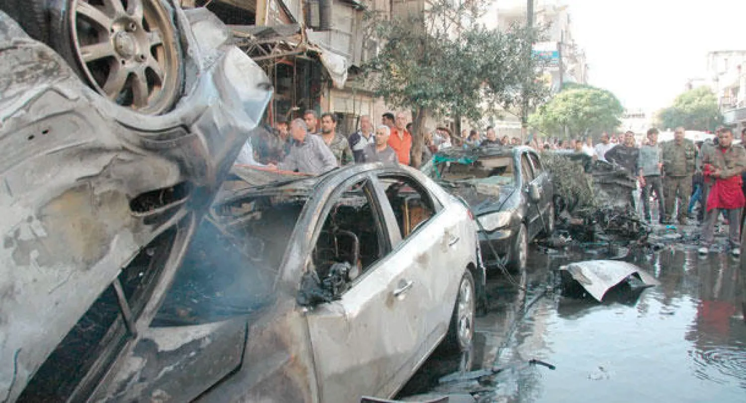 سوريون يتجمعون حول حطام خلفه تفجير سيارتين مفخختين بمنطقة كرم اللوز في مدينة حمص أول من أمس (رويترز)