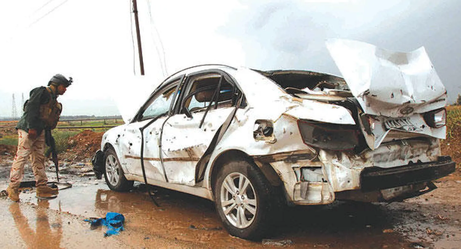 عنصر أمن عراقي يعاين سيارة متضررة في موقع انفجار غرب كركوك أمس (رويترز)